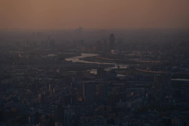 A hazy aerial view of a sprawling metropolis with a winding river at dusk