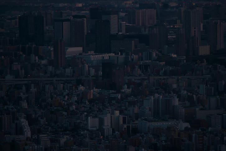 A static aerial view of a dense, sprawling cityscape settling into the deep blue of night