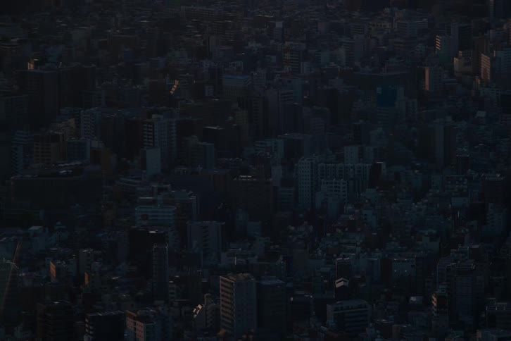 A vast and dark urban cityscape is seen from a high angle as the sun sets