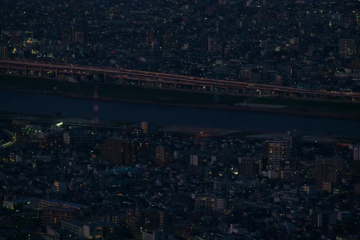 Time-lapse of nighttime traffic on a highway alongside a river, set against the backdrop of a sprawling, illuminated cityscape