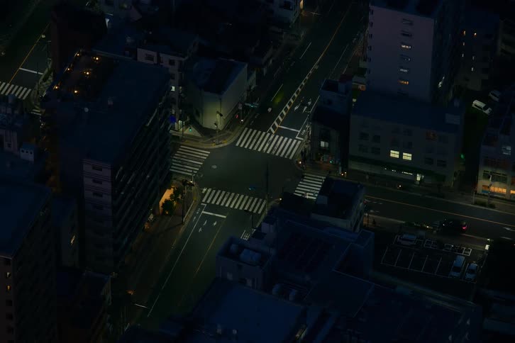 An aerial view captures the quiet, late-night traffic passing through a dimly lit city intersection
