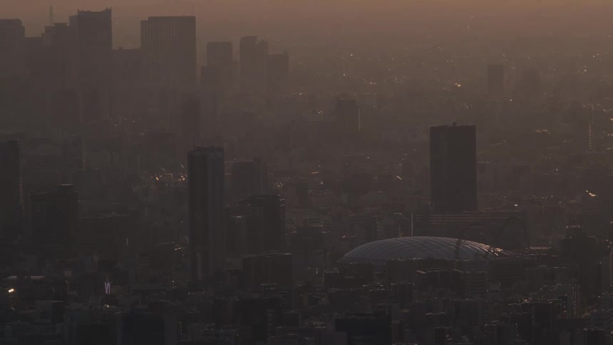 A vast, hazy cityscape with a domed stadium is bathed in the warm, muted light of sunset
