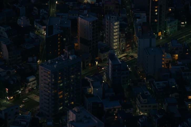 An overhead view of a dense city neighborhood at night with traffic moving through the illuminated streets