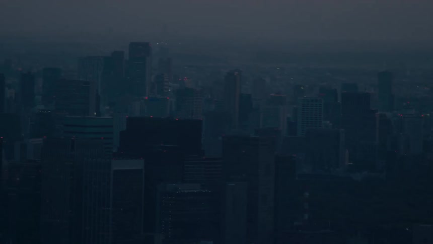 Mount Fuji is silhouetted against the sunset sky before the camera pans down to reveal the sprawling Tokyo cityscape at dusk