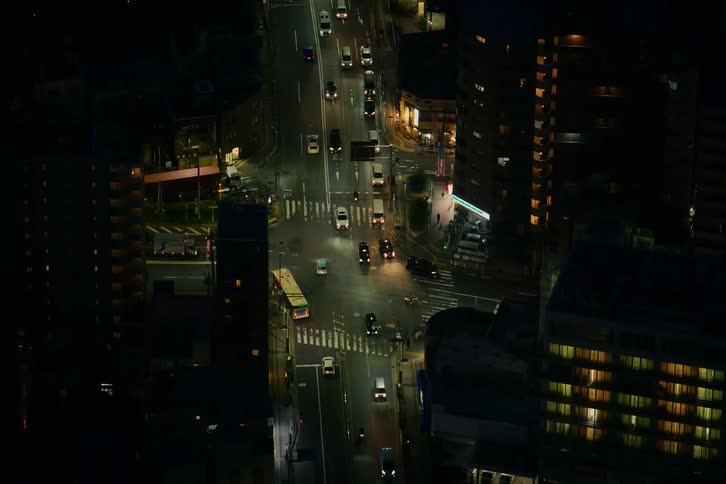 An aerial view of a city street intersection shows the flow of traffic late at night