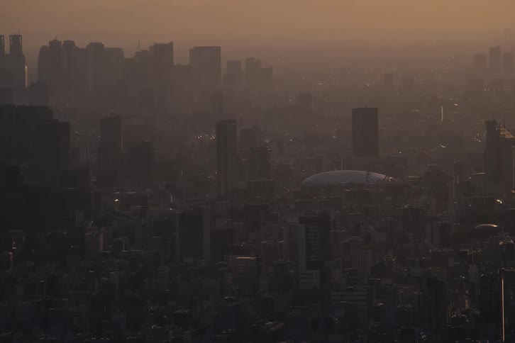 An expansive, hazy cityscape with a large dome is silhouetted against the golden light of a setting sun