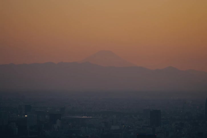 The majestic silhouette of Mount Fuji looms over the sprawling Tokyo cityscape during a warm, hazy sunset