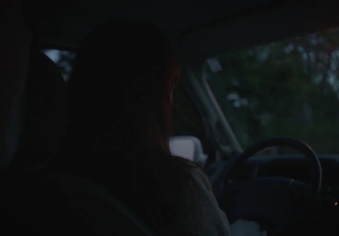Over-the-shoulder view of a woman driving a van through a suburban neighborhood at dusk