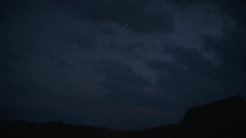Glowing embers from a bonfire float up into the cloudy twilight sky