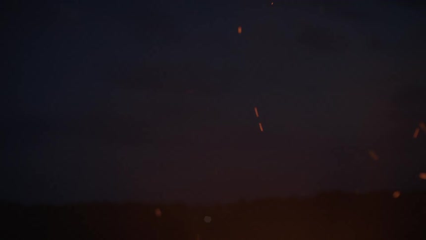 Golden embers and sparks rise from a bonfire against the backdrop of a dark evening sky