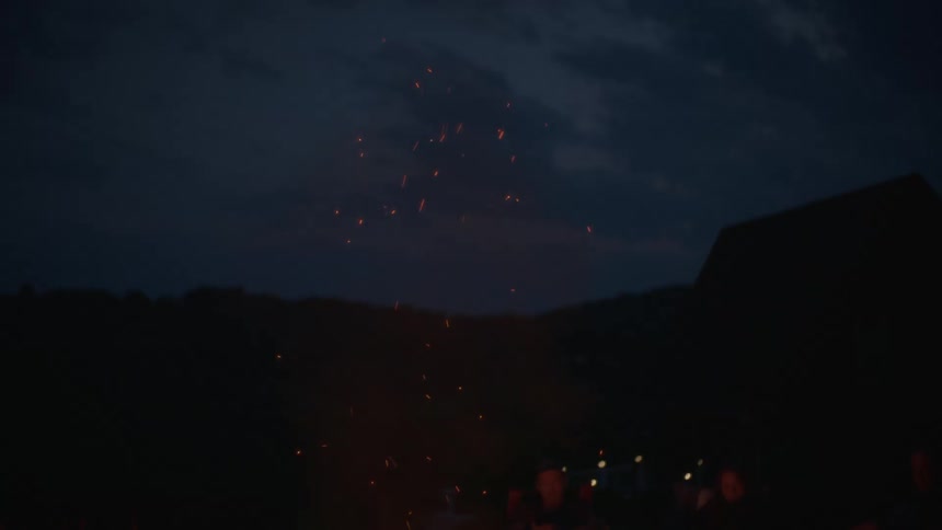 Embers from a campfire rise into the evening sky as a group of friends relax together in the peaceful outdoors