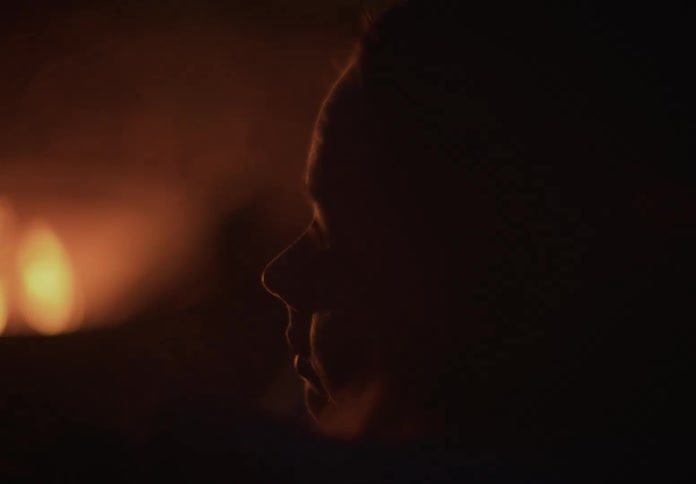 Close up silhouette of a person's face is illuminated by a flickering fire in the dark