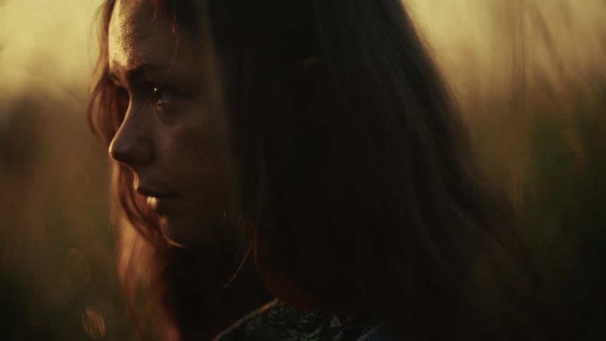 A close-up profile of a sad young woman in a golden field at sunset as the camera slowly comes into focus