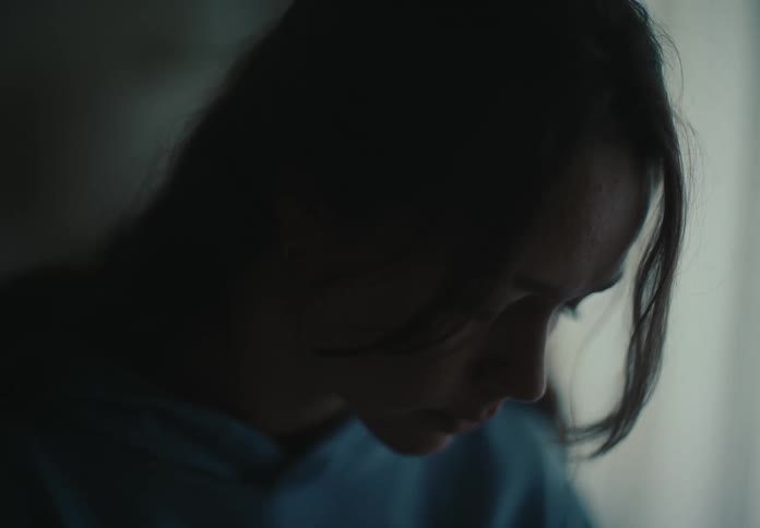 Dramatic close-up profile of a sad and contemplative woman's face, her head bowed in a dimly lit room