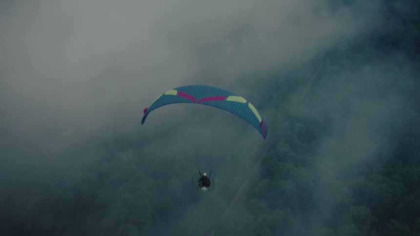 A colorful paraglider soars through the misty clouds above a dense jungle landscape