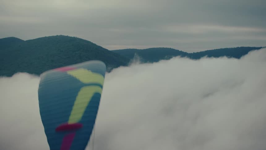 A paramotorist in slow motion soars peacefully above a thick blanket of clouds covering a mountain range