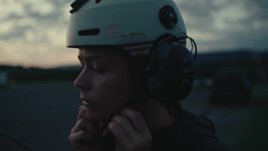 A focused young woman in slow motion puts on her communications helmet and headset at dusk