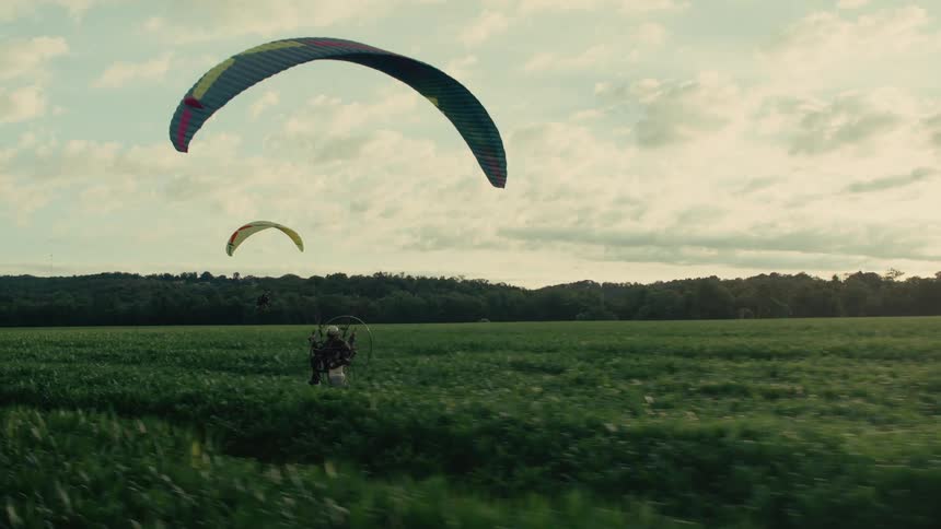 Following a powered paraglider as they run through a vibrant green field attempting to take flight at sunset