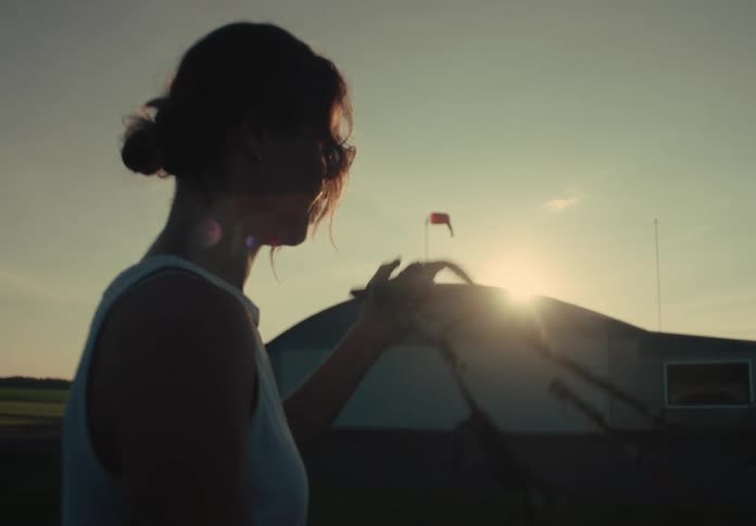 A silhouetted woman walks across a rural airfield with her hang gliding equipment as the sun sets