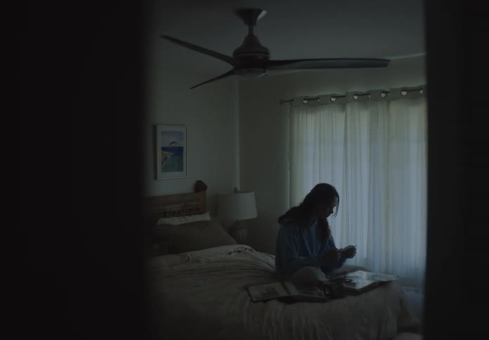 Slow reveal shot of a pensive young woman sitting on her bed looking through a scrapbook of old photos