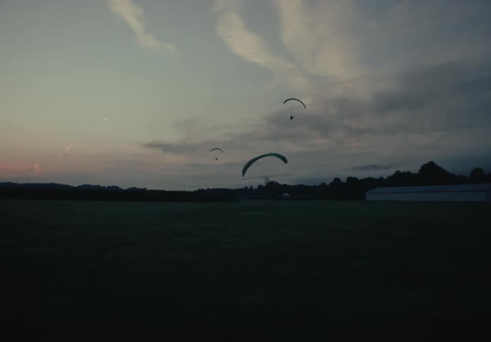 Several powered paragliders fly low across a grassy airfield during a beautiful, serene twilight