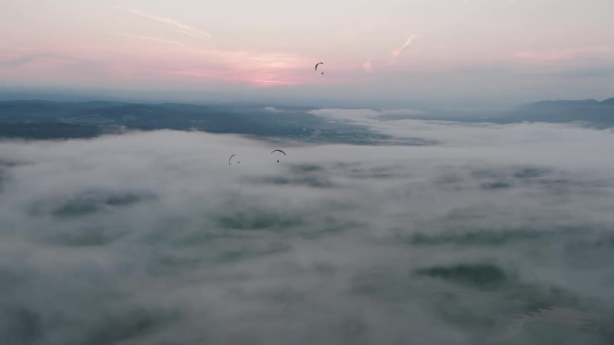 Three paragliders peacefully soar above a dreamy sea of fog at sunrise