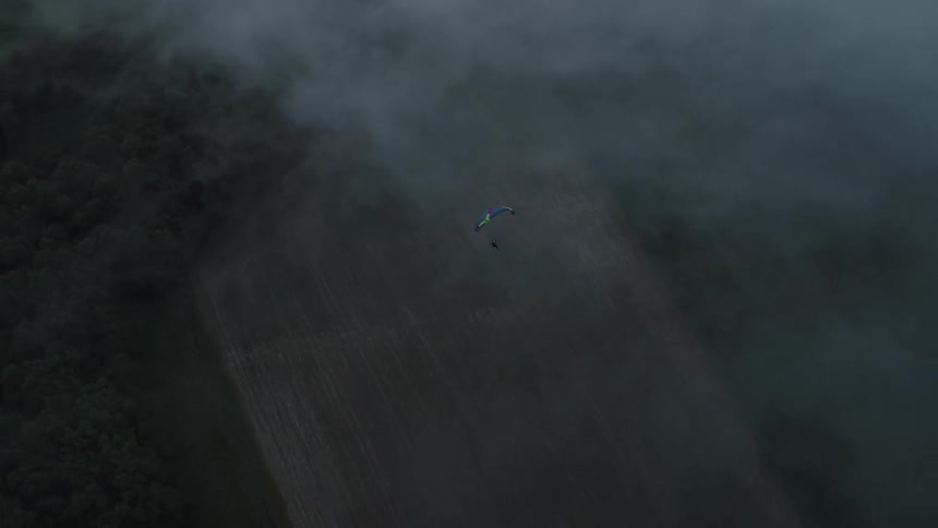 An aerial view shows a lone paraglider peacefully gliding through a thick blanket of fog over a rural landscape