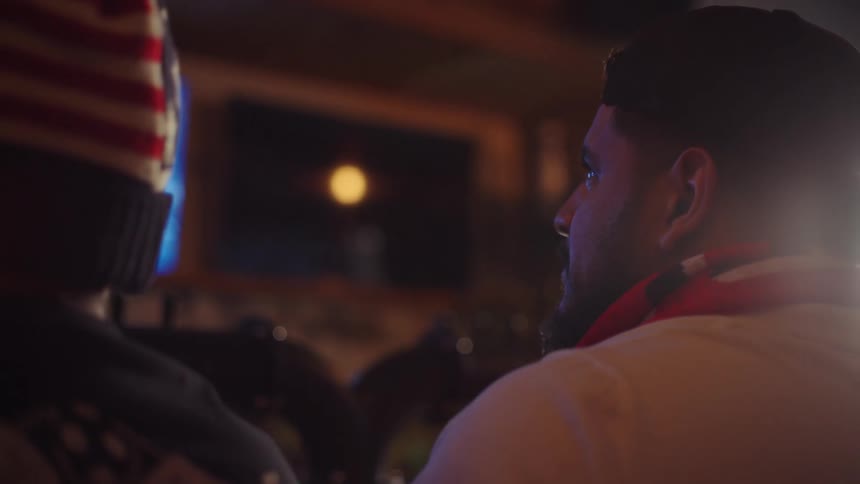 Two sports fans intently watch a game on a television in a dimly lit room