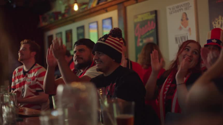 A diverse group of patriotic American sports fans joyfully clap and cheer for their team in a pub