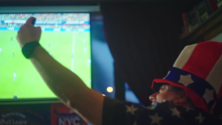 A patriotic man in an American flag hat takes a selfie with his friends at a sports bar while watching a soccer match