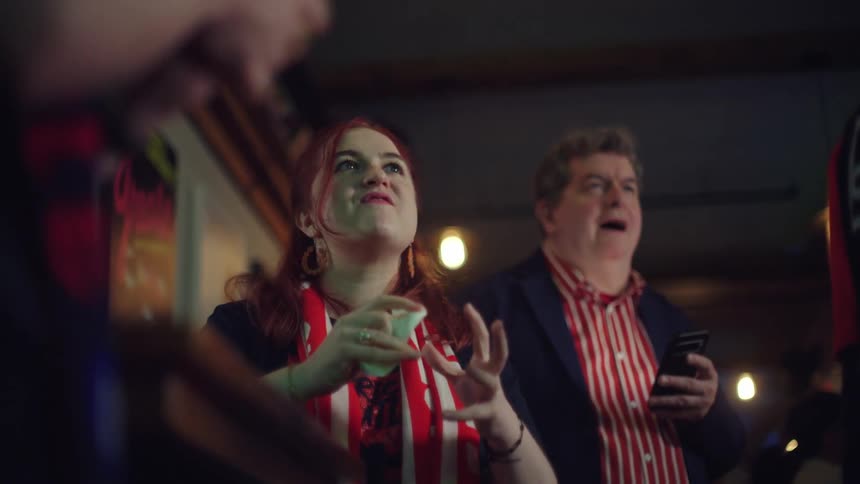 A young woman with red hair nervously eats a french fry and watches a sports game in a bar in slow motion