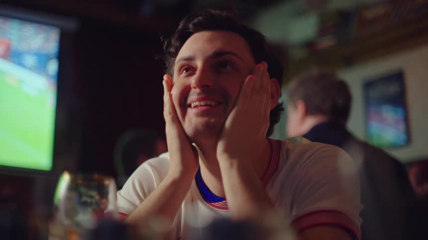 A tense sports fan watching a game at a pub transitions from deep disappointment to overwhelming joy and relief in a single moment