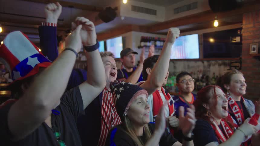 Patriotic fans wearing red, white, and blue go wild with excitement, cheering and clapping in a sports bar