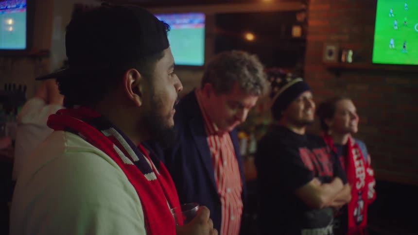A diverse group of happy sports fans toast with drinks and enjoy watching a soccer match together at a local bar