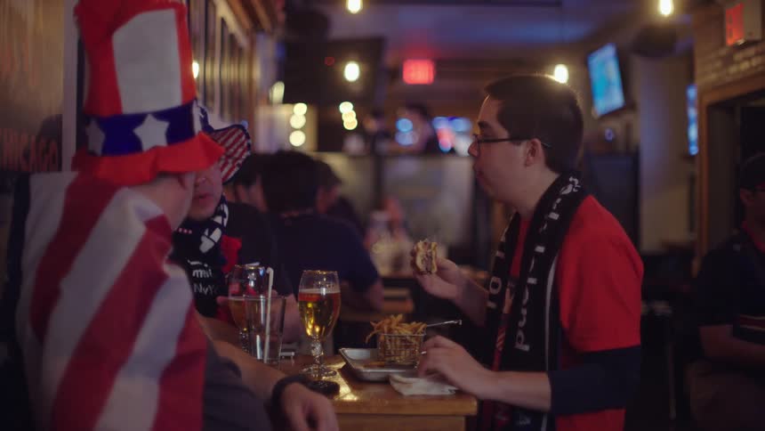 Patriotic sports fans eat, drink, and socialize together in a dimly lit sports bar