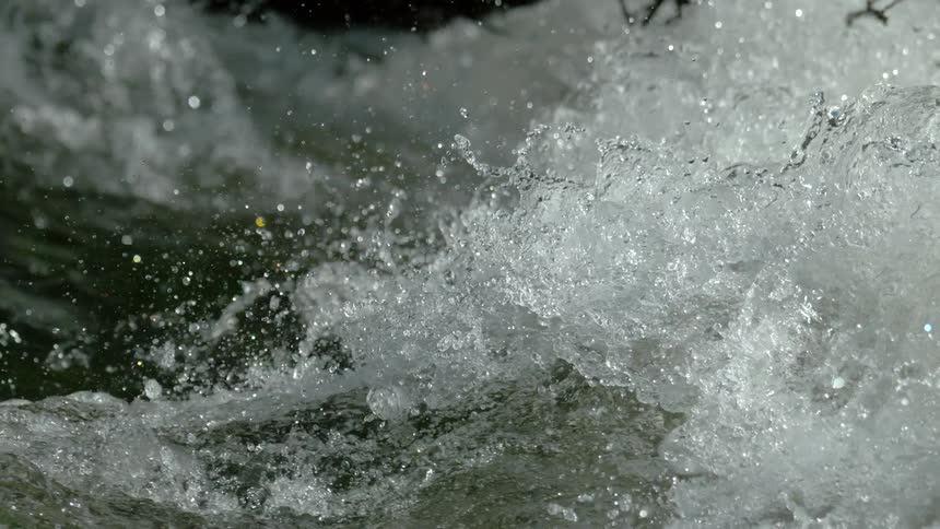 An extreme slow-motion close-up shot captures the turbulent and powerful splashing of whitewater rapids