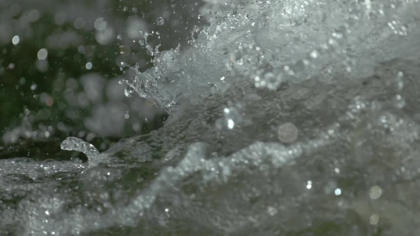 An extreme close-up of whitewater splashing and bubbling in super slow motion as glistening droplets fly through the air
