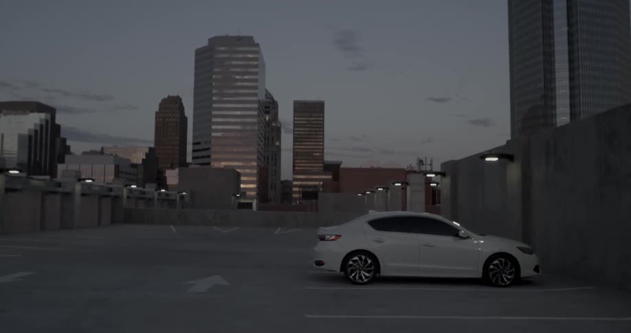 A white car parked in a parking lot under a street light in a large city