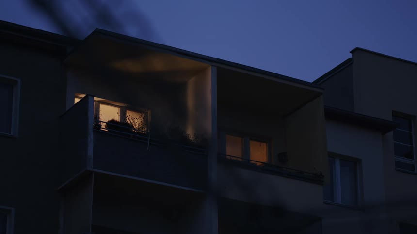 Warm lights glow from windows of a building balcony in the evening light