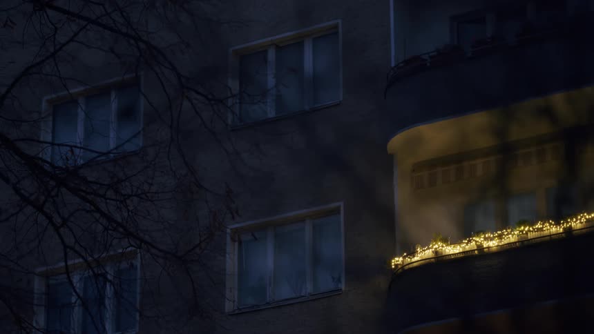A lone apartment balcony glows with festive string lights against the dark facade of a building on a quiet night
