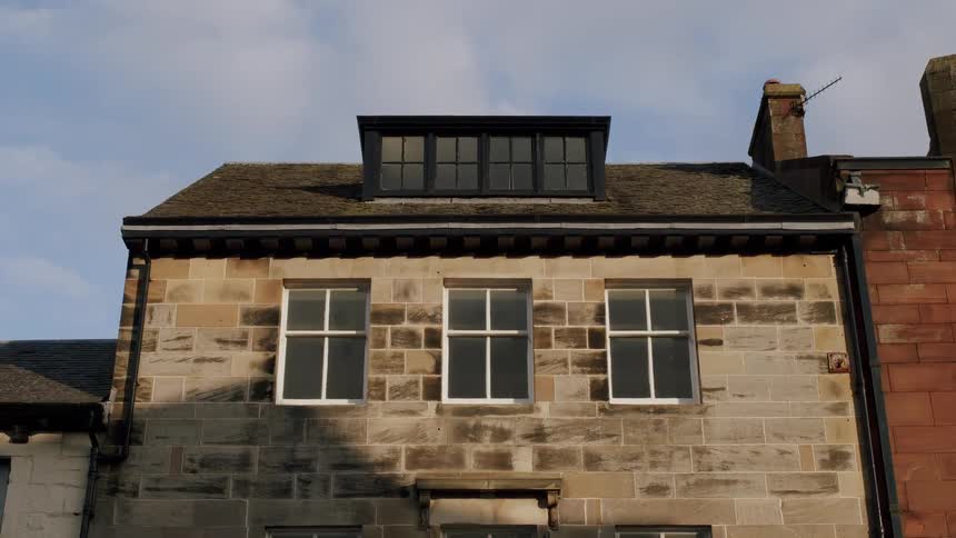 A seagull soars past an old stone building in slow motion on a sunny day