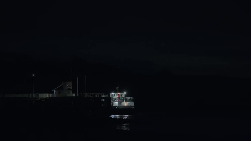 A solitary boat docked at a pier offers a glimmer of light against the deep darkness of night