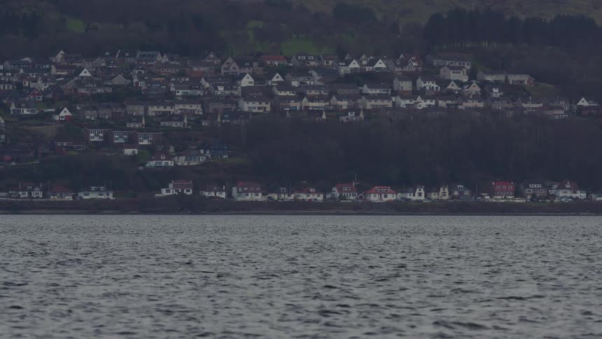 A scenic view of a coastal town built on a hill, seen from across the water on a gray, overcast day