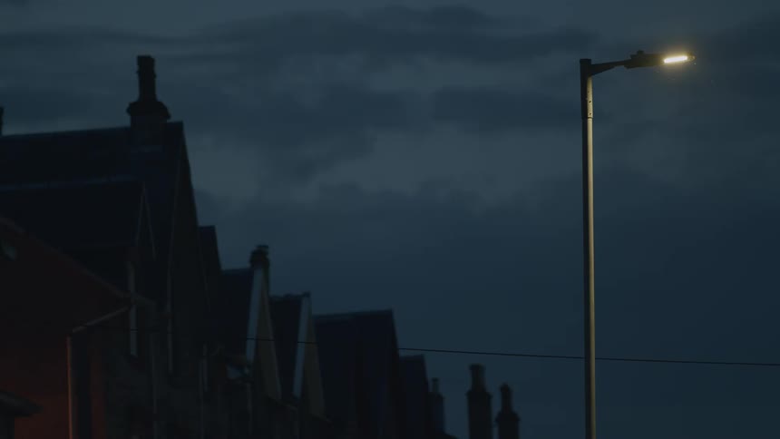 A lone street lamp illuminates a row of houses on a dark and cloudy night