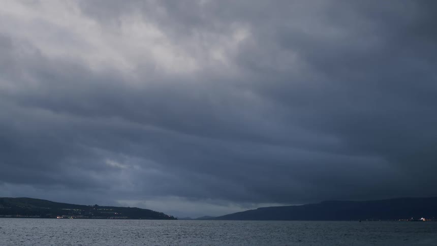 A moody, dramatic shot of dark, heavy storm clouds gathering over a wide expanse of water at dusk