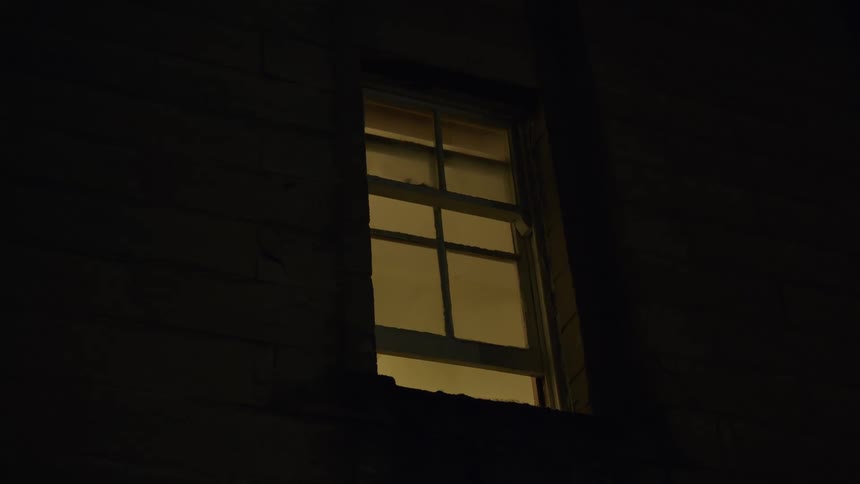 A single illuminated window shines with a warm yellow glow from a dark building at night