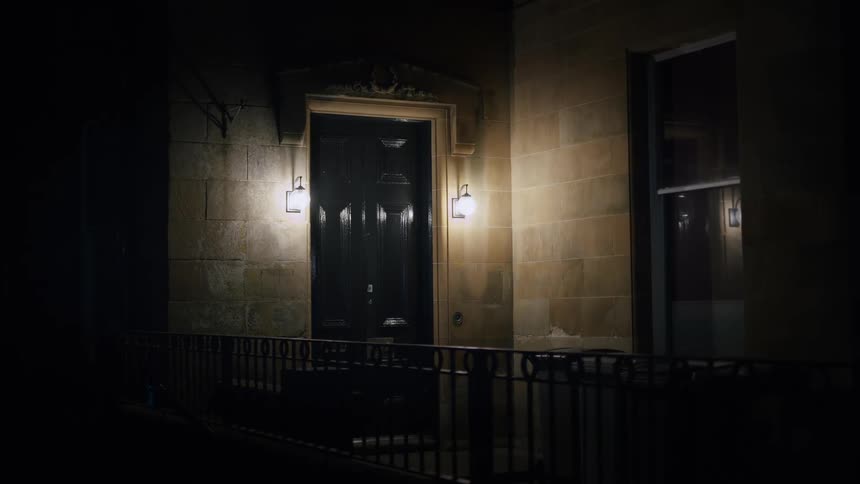The entrance to a city townhouse is lit by two wall sconces on a dark night