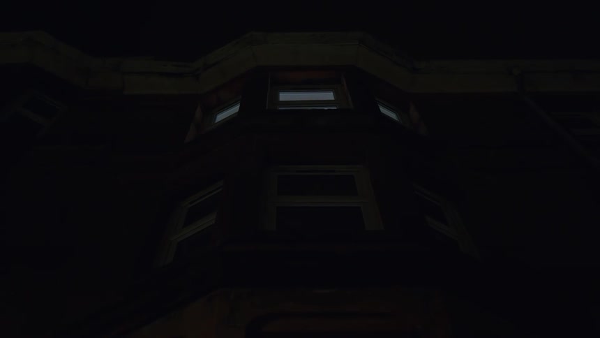A mysterious light flashes repeatedly in the upper window of a dark building at night
