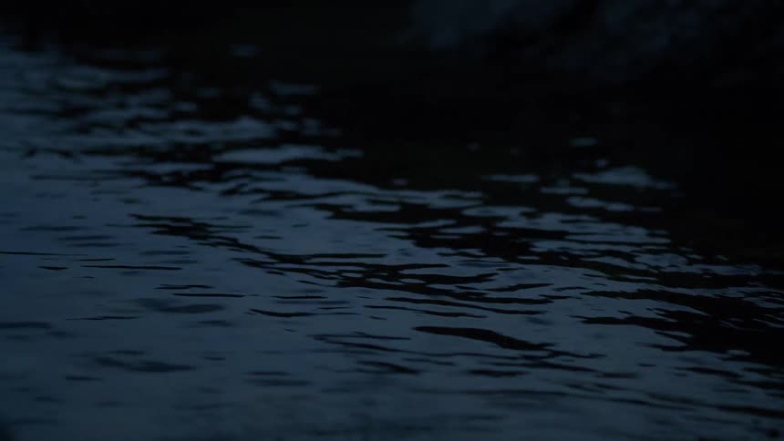 A close-up view of dark, rippling water at night, creating a calm and moody atmosphere