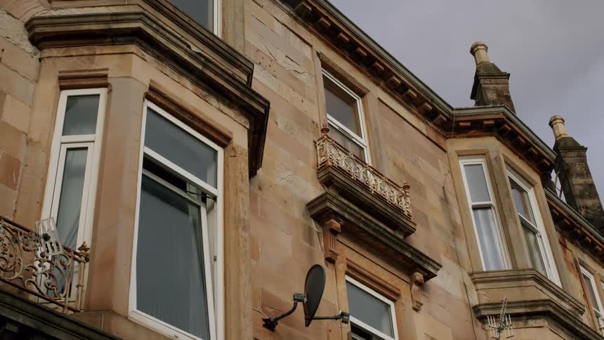 A low angle shot of a traditional sandstone tenement building facade on an overcast day